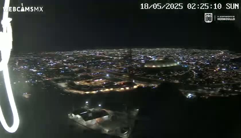 A nighttime, high-angle view of a sprawling city illuminated by lights, seen from a vantage point above.