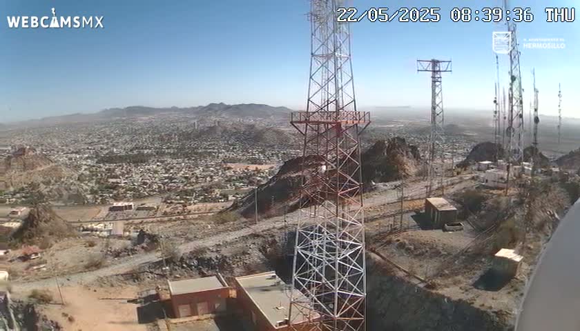 On a clear day, a high vantage point shows numerous communication towers on a rocky hillside overlooking a sprawling city.