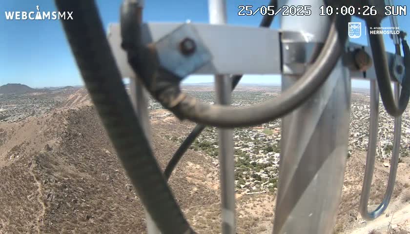 A view from a tall metal structure on a sunny day shows a sprawling desert town nestled against a rocky hillside.