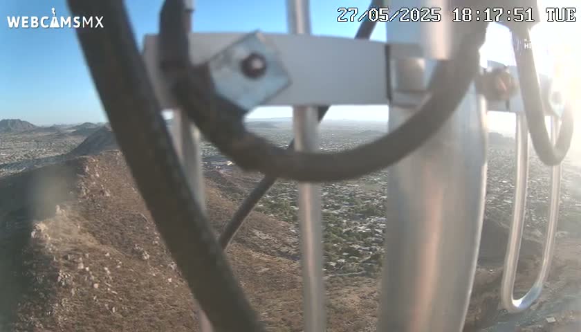 A view of a sprawling city and desert landscape is partially obscured by a metal antenna structure on a clear, sunny day.