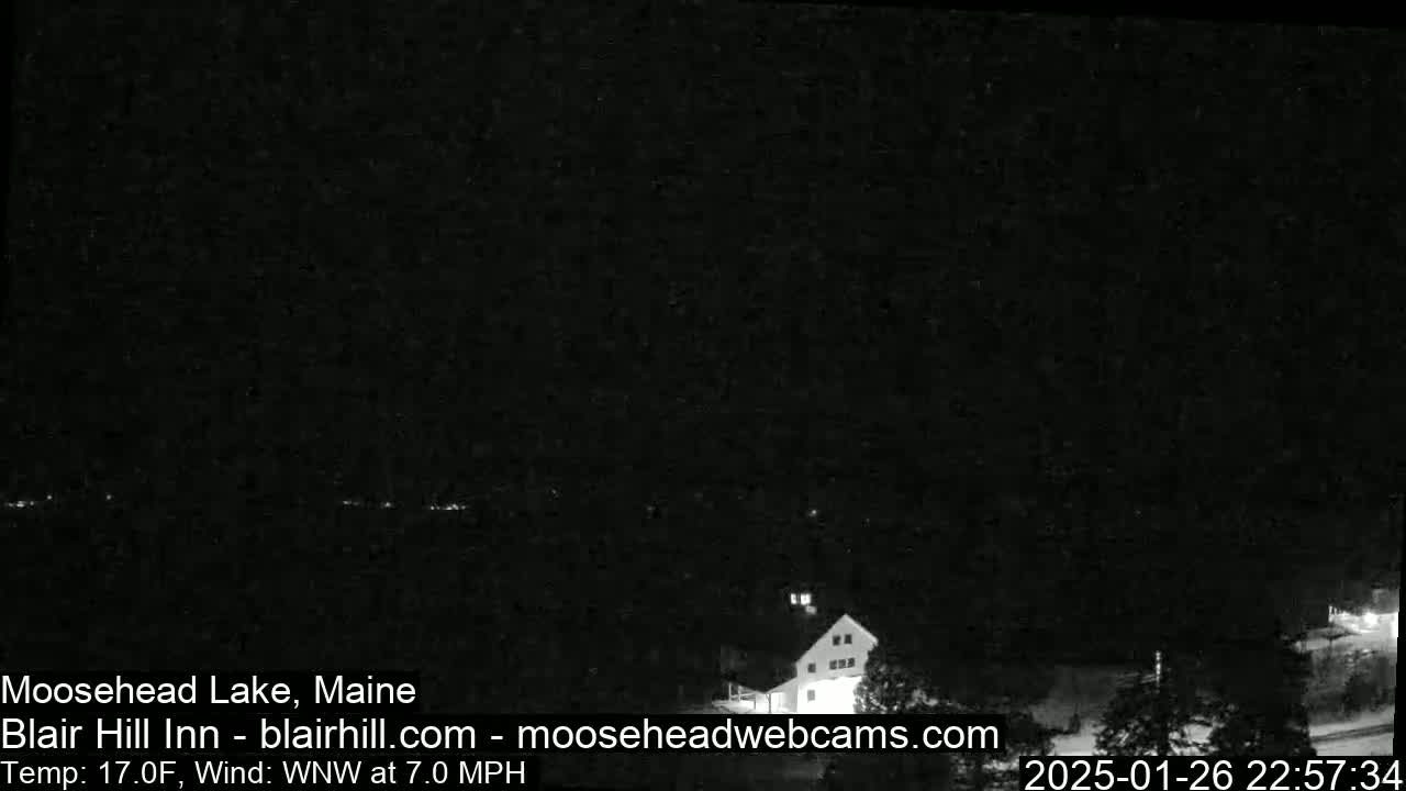 A nighttime view of a lake and a building under a dark, clear sky with a 7 mph wind.