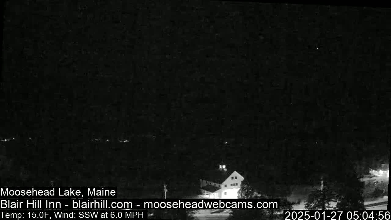 A nighttime, low-light image shows a building and surrounding trees under a dark, clear sky with a temperature of 15°F and a south-southwesterly wind.