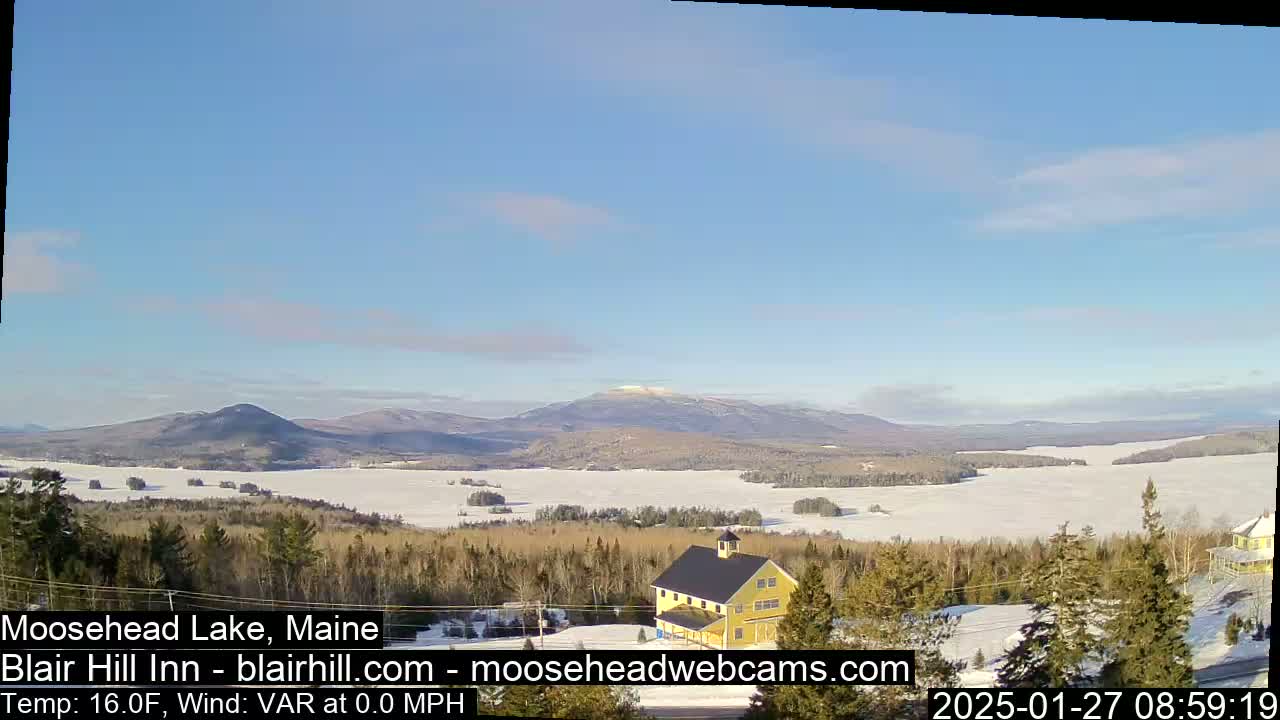 A snow-covered lake and distant mountains are visible under a clear blue sky, with a yellow building in the foreground.