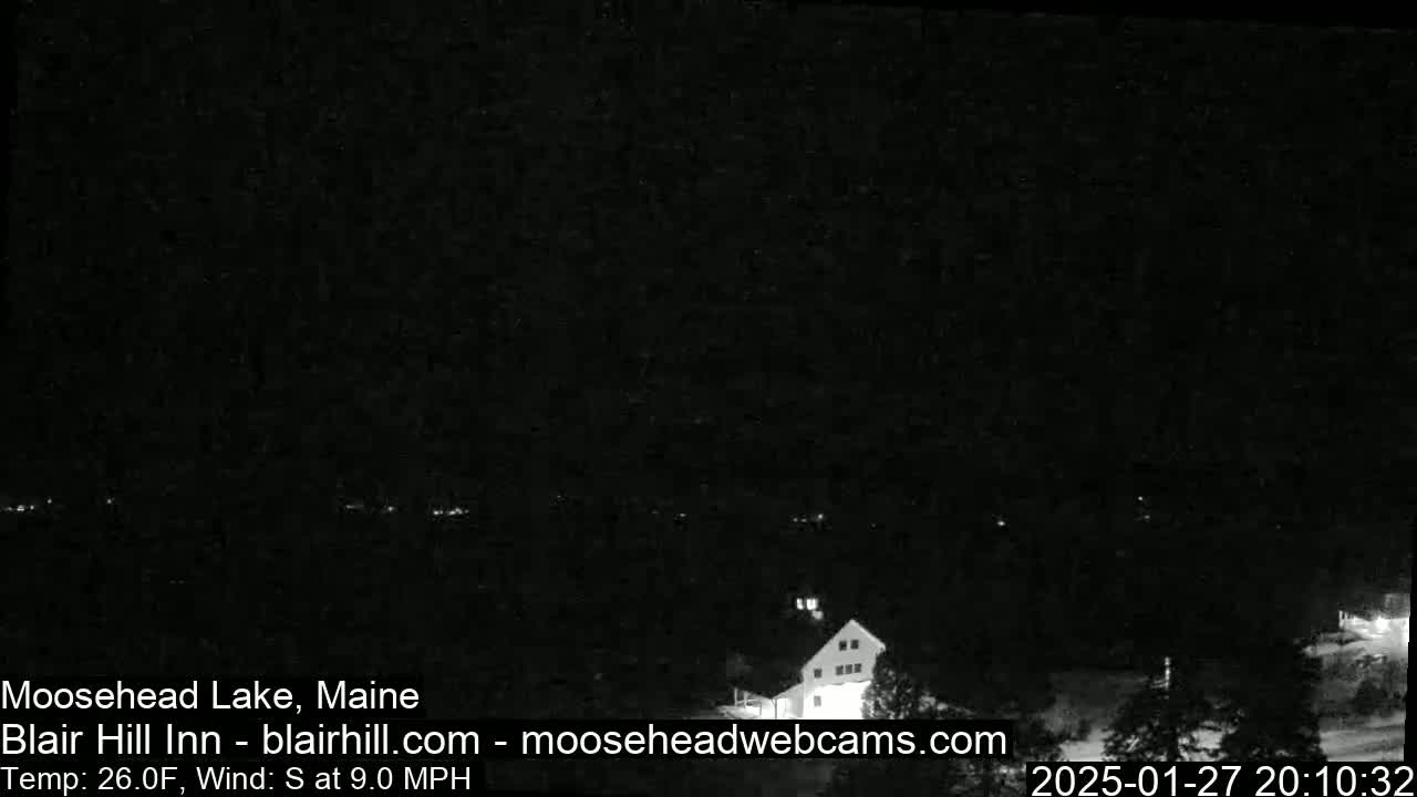 A nighttime, low-light view of a building near a lake under a dark sky with a south wind at 9 mph and a temperature of 26°F.