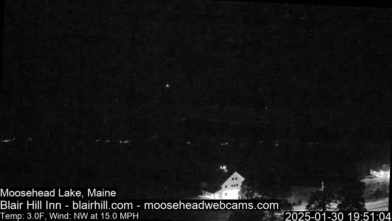 A nighttime view of a lake and a building under a dark sky with a northwest wind at 15 mph and a temperature of 3°F.