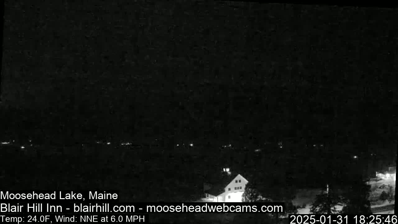 A nighttime view of a dark lake with a few lights visible along the shoreline and a building illuminated on the right.