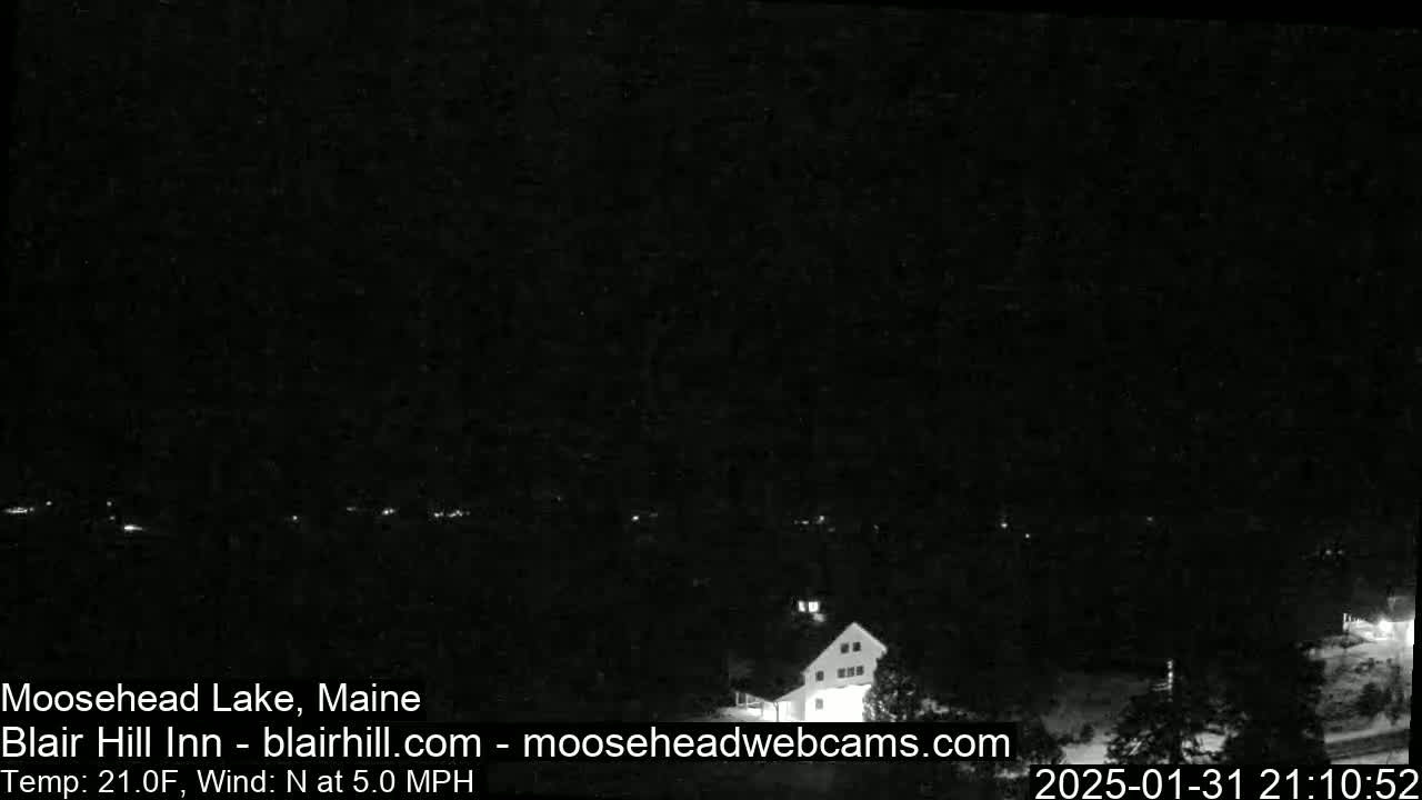 A nighttime view of a lake and a building, with a north wind at 5 mph and a temperature of 21 degrees Fahrenheit.