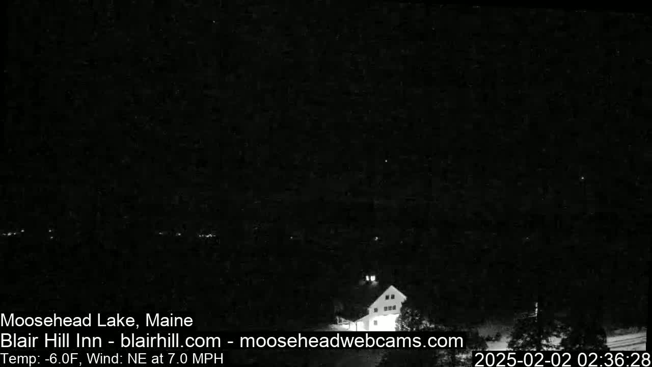 A dark nighttime scene shows a building and trees under a clear sky with a northeast wind at 7.0 mph and a temperature of -6°F.