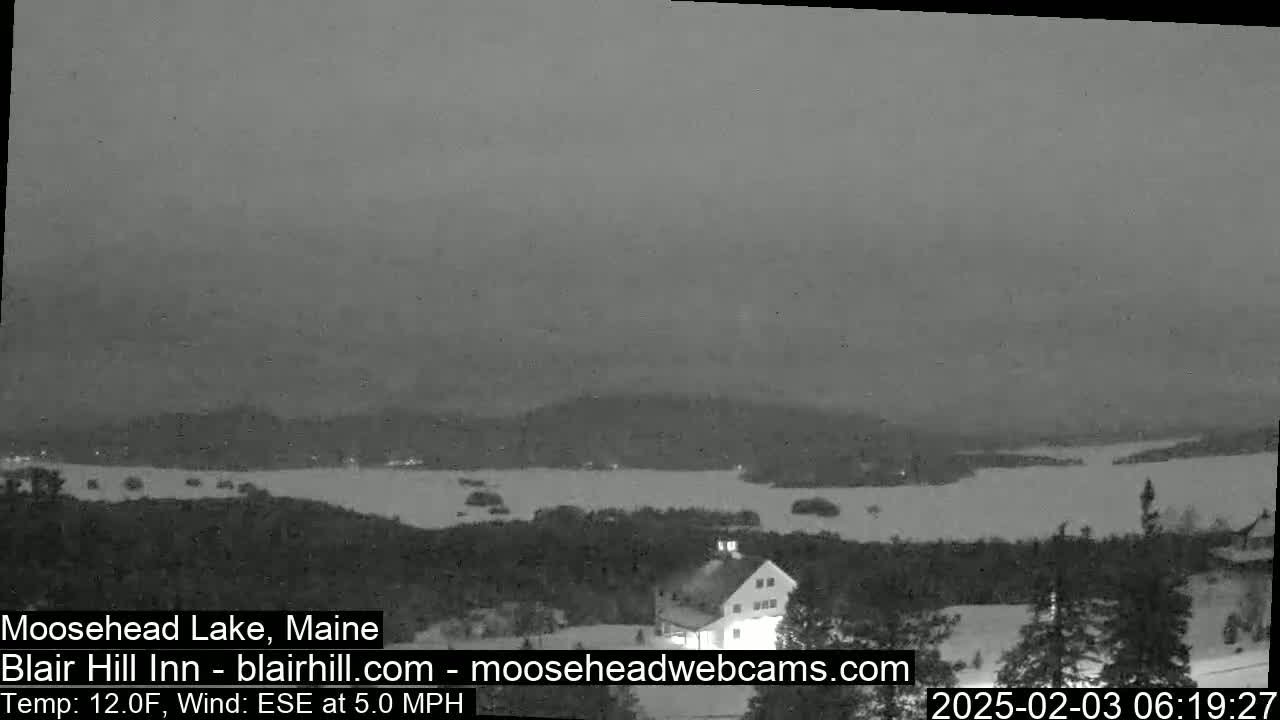 A snow-covered landscape at night overlooks a dark lake under a cloudy sky with a 5 mph wind and a temperature of 12°F.