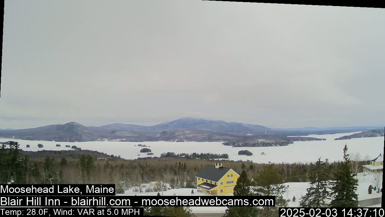 A snow-covered lake and distant mountains are visible under an overcast sky.
