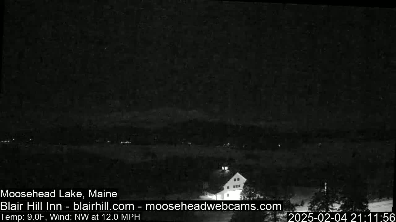 A nighttime, low-light view of a building and a distant, dimly lit landscape under a dark sky with a northwest wind at 12 mph and a temperature of 9°F.