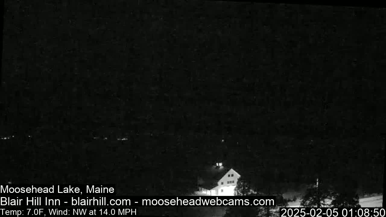 A dark, nighttime image shows a building and trees under a clear sky with a northwest wind at 14 mph and a temperature of 7 degrees Fahrenheit.