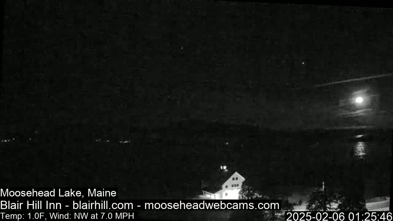 A nighttime view of a lake and a building under a bright moon and a partly cloudy sky.