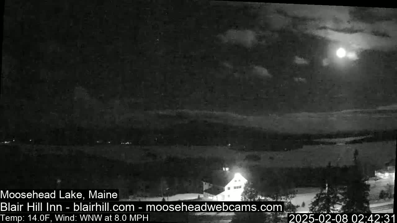 A nighttime view of a lake and a building under a partly cloudy sky with a bright moon.