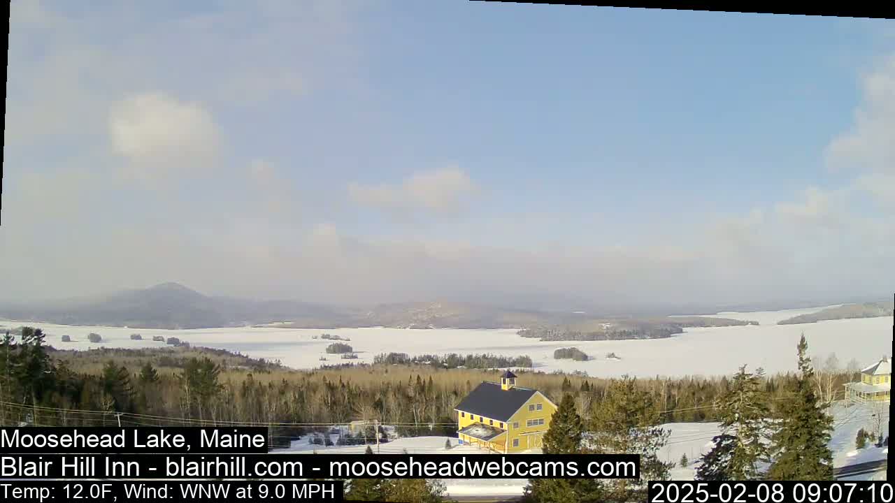 A snow-covered lake and forested landscape are visible under a partly cloudy sky, with a yellow building situated in the foreground.
