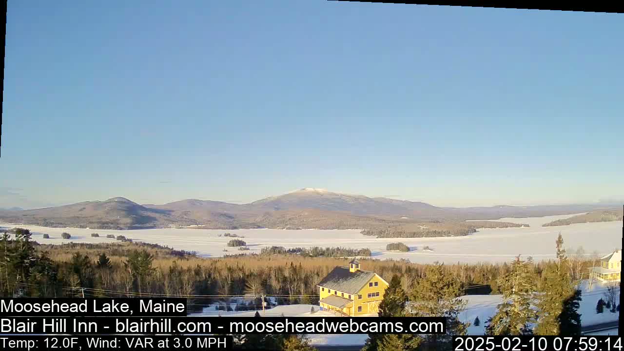 A frozen lake and snow-covered landscape stretch towards distant mountains under a clear blue sky.