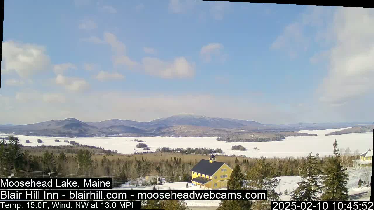 A partly cloudy, cold day shows a frozen lake, a yellow building, and distant mountains.