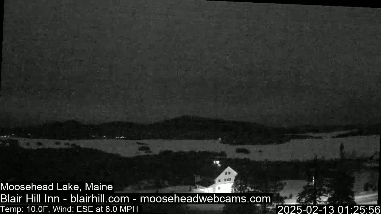 A nighttime view of a snow-covered landscape, including a body of water and a building, under a dark sky with an 8 mph wind and a temperature of 10 degrees Fahrenheit.