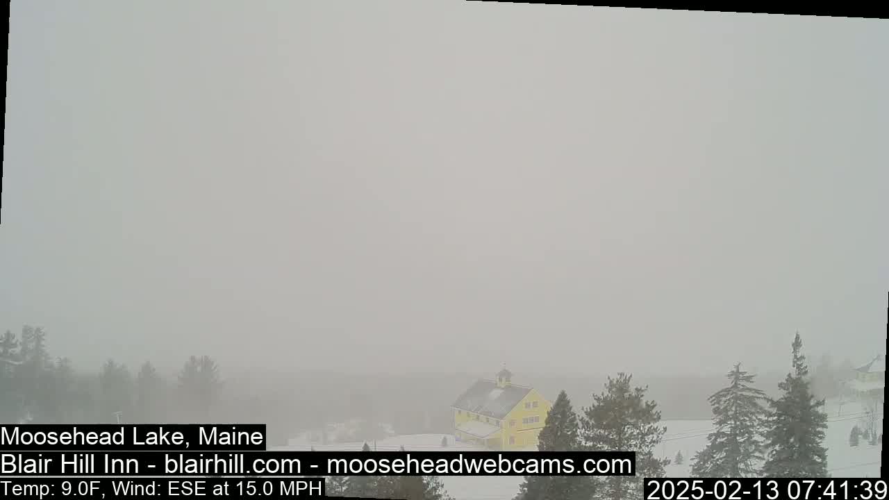 A yellow building is partially visible through heavy snow and fog in a snowy landscape.