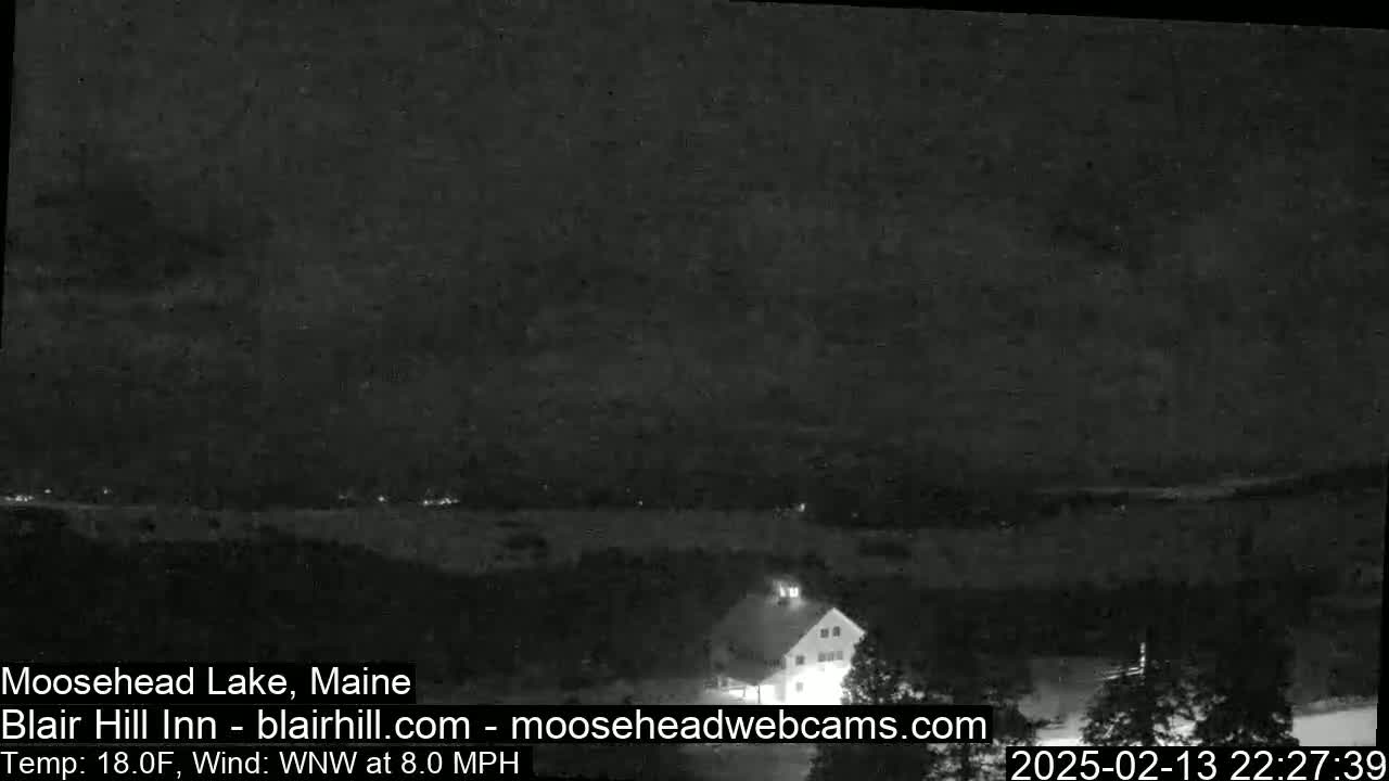 A nighttime view of a lake and a building under a dark, cloudy sky with a wind blowing from the west-northwest at 8 miles per hour and a temperature of 18 degrees Fahrenheit.