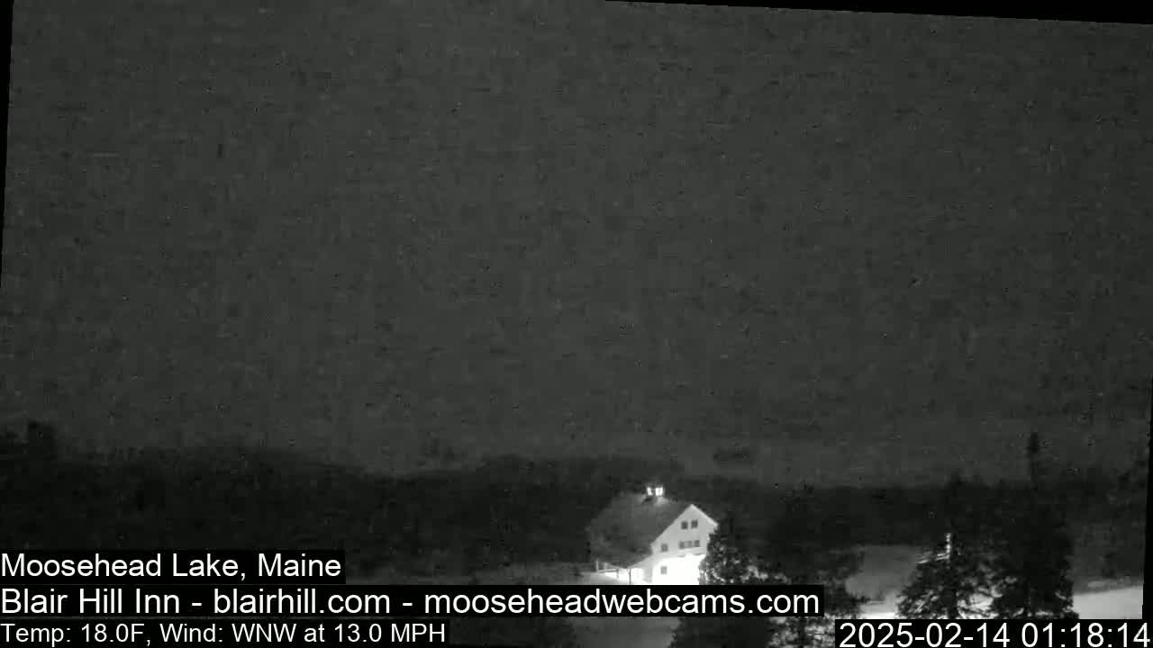 A dark, nighttime view of a building in a snowy landscape with a WNW wind at 13.0 mph and a temperature of 18.0°F.