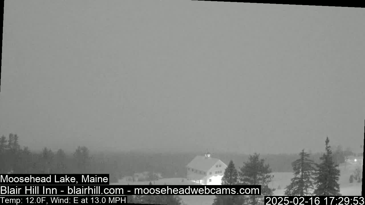 A snow-covered landscape with a building and trees is visible under a heavily overcast sky, with an east wind at 13 mph and a temperature of 12°F.