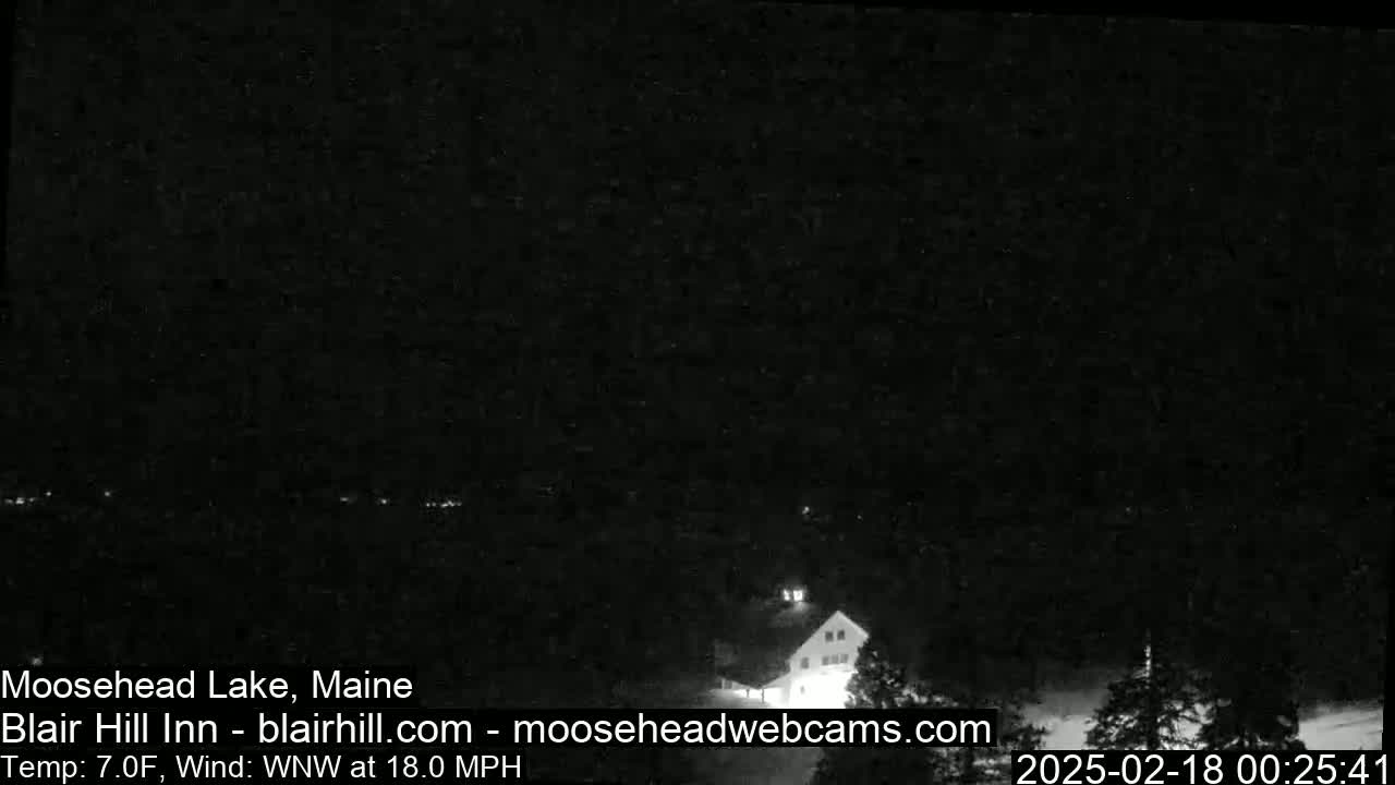 A dark, nighttime view of a building near a lake under a clear sky with a 7°F temperature and a 18 mph wind from the west-northwest.