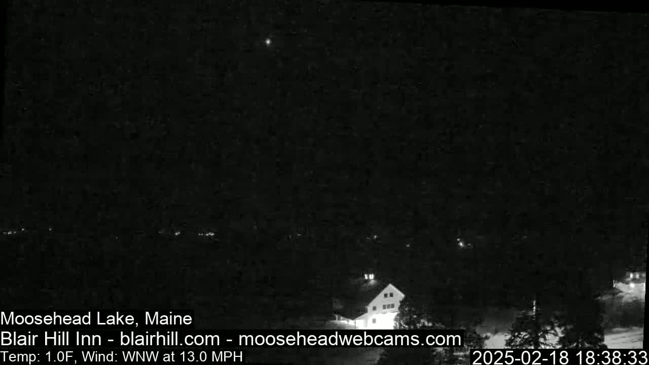 A nighttime, low-light view of a building and surrounding trees under a clear sky with a 13 mph wind.