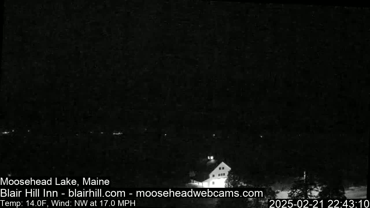 A dark nighttime scene shows a building and some lights in the distance, with a northwest wind at 17 mph and a temperature of 14 degrees Fahrenheit.