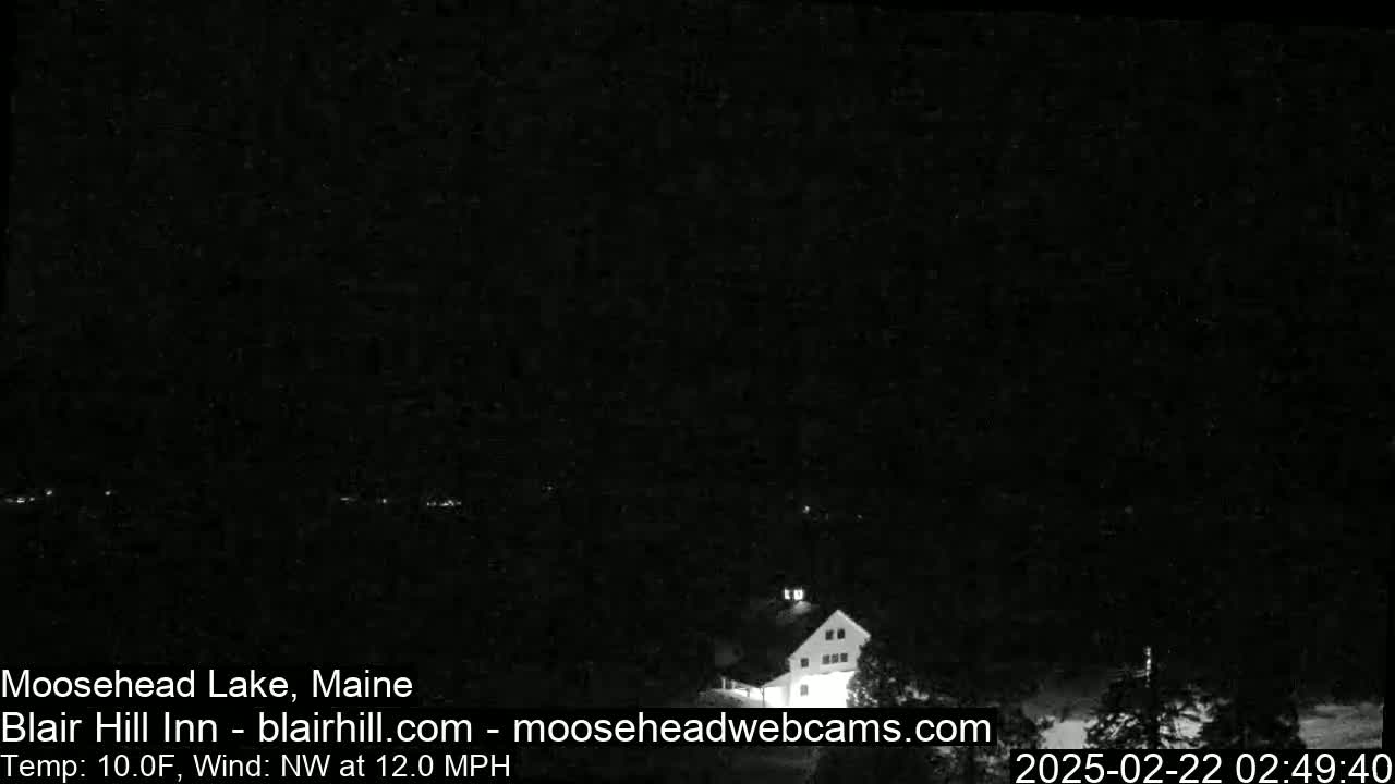 A dark nighttime scene shows a building with lights on near a lake under a clear, dark sky with a northwest wind.