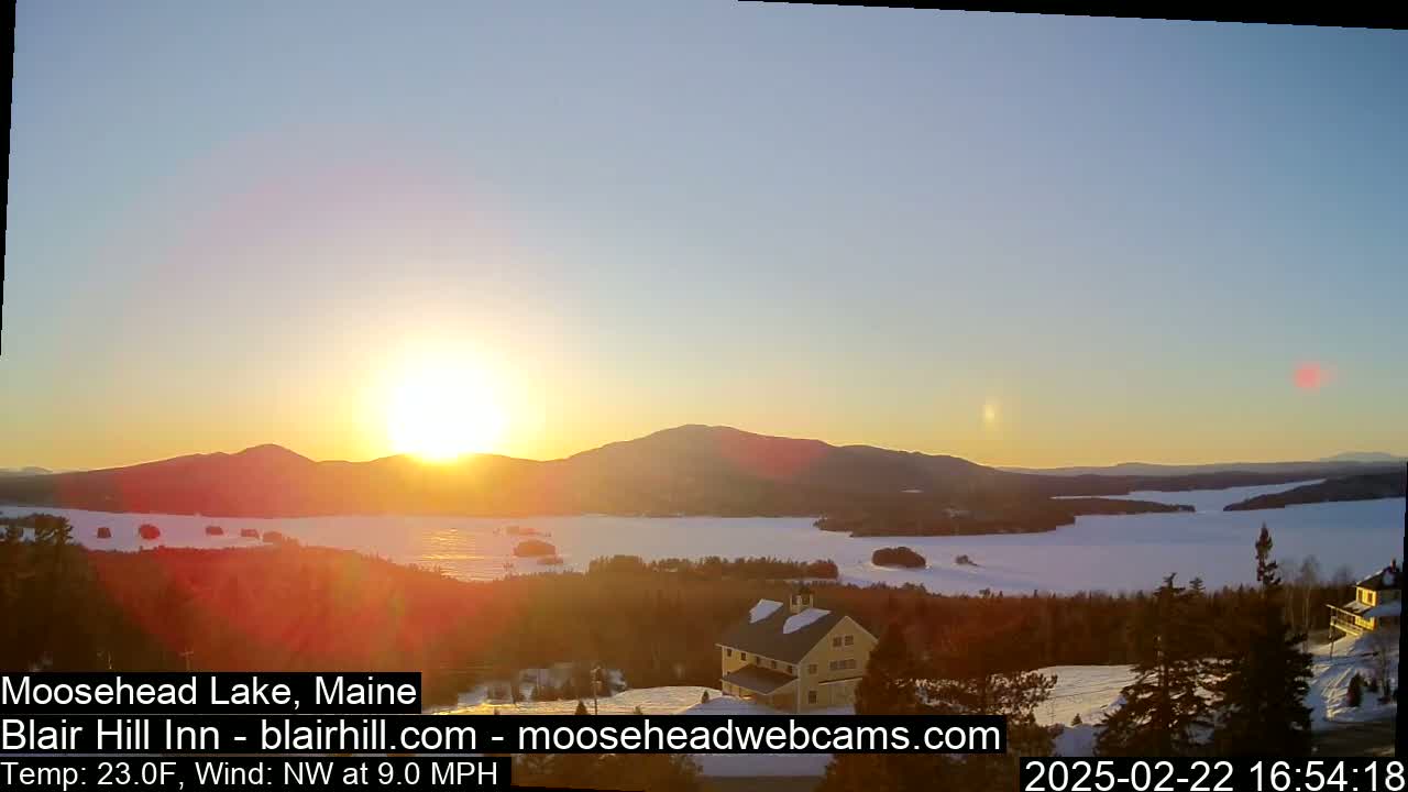 A winter sunset over a snow-covered lake and mountains, with a building visible in the foreground.