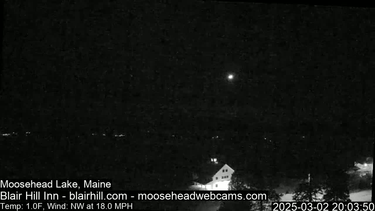 A nighttime, snow-covered landscape with a building illuminated under a bright moon and a northwest wind blowing at 18 mph in 1-degree Fahrenheit weather.