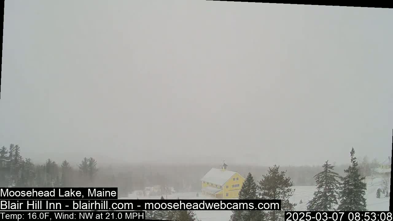 A yellow barn is partially visible in a snowy landscape under heavy overcast conditions.