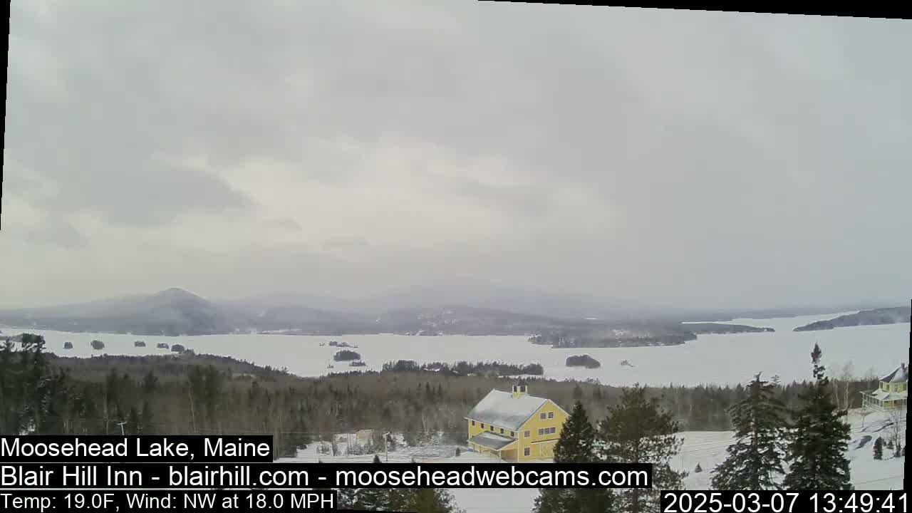 A snow-covered landscape overlooks a frozen lake under an overcast sky.