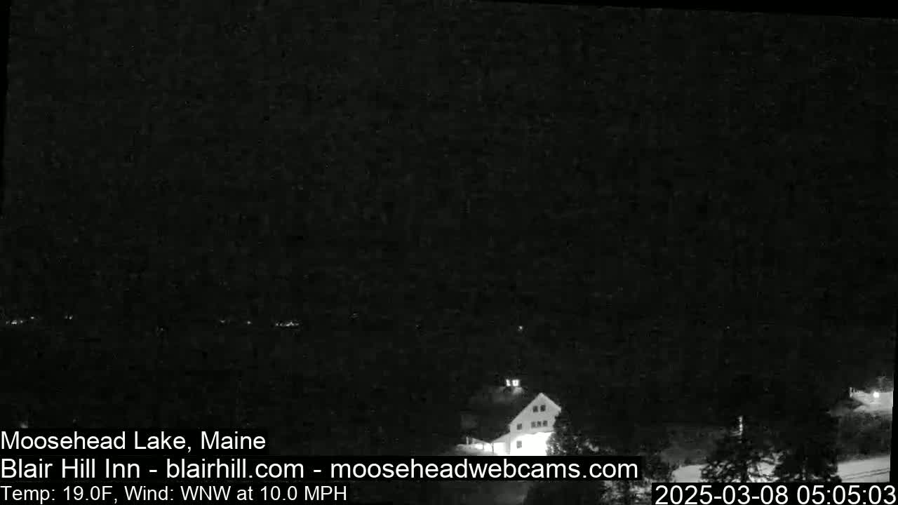 A dark nighttime scene shows a building and some trees under a clear sky with a WNW wind at 10 mph and a temperature of 19°F.