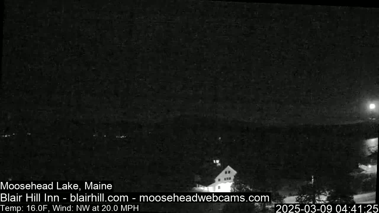 A nighttime, low-light view of a lake and a building under a mostly clear sky with a northwest wind at 20 mph and a temperature of 16°F.