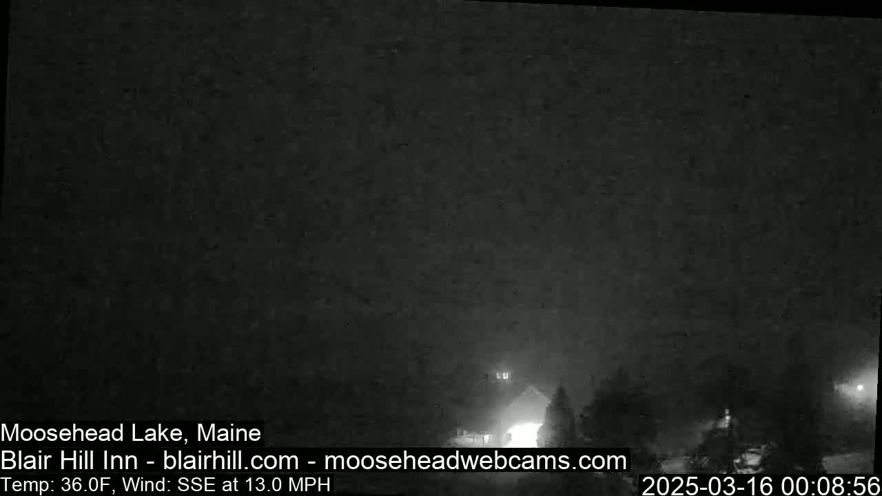 A dark, nighttime scene with hazy or foggy conditions and a building faintly visible in the distance under a mostly clear sky; the wind is blowing from the south-southeast at 13 mph.