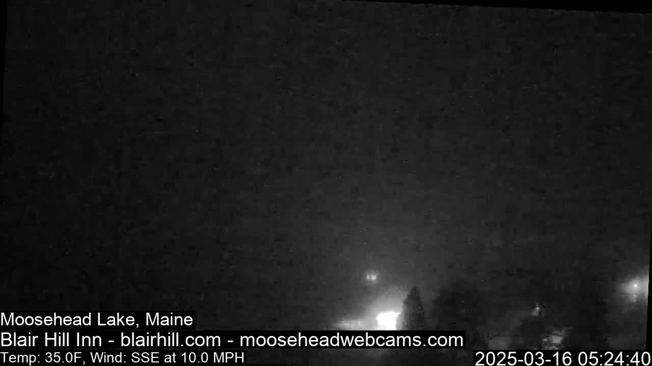A dark, nighttime scene with some faint light sources in the distance, under a mostly clear sky, and a wind blowing from the south-southeast at 10 mph.