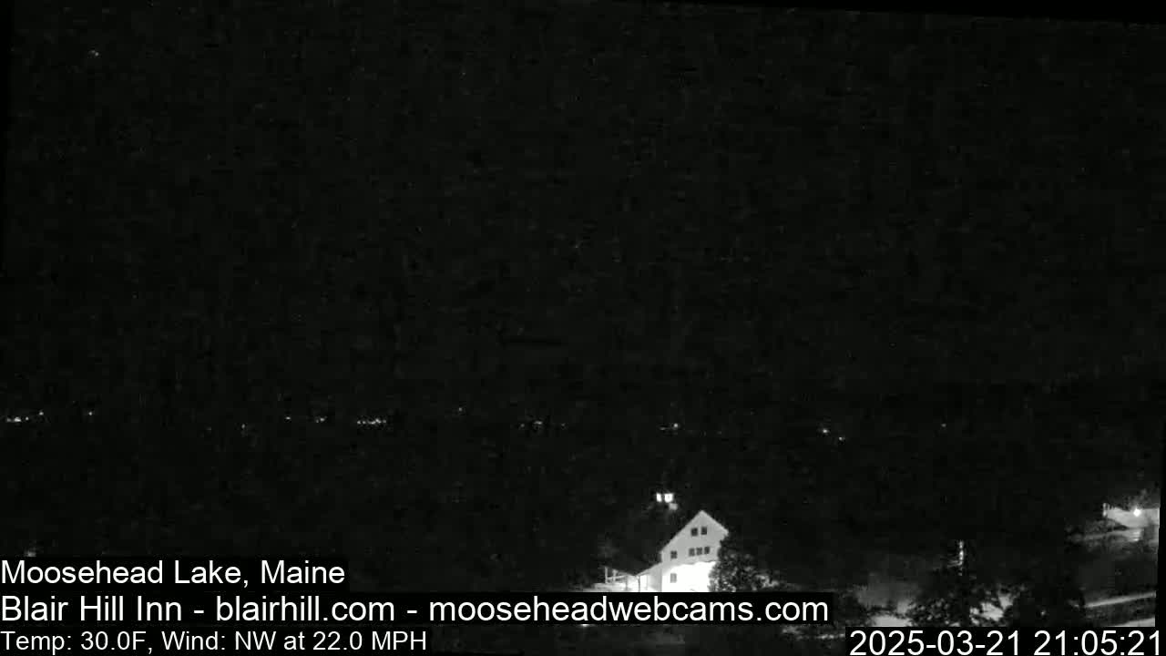 A nighttime view of a building near a lake under a dark, clear sky with a northwest wind at 22 mph and a temperature of 30°F.