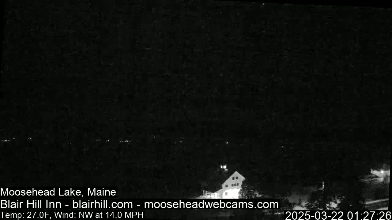 A dark nighttime scene of a lake and a building, with a northwest wind at 14 mph and a temperature of 27 degrees Fahrenheit.