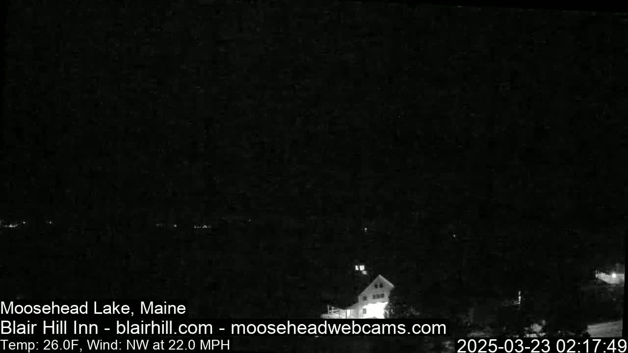 A dark, nighttime scene of a building partially visible among trees under a dark sky with a northwest wind at 22 mph and a temperature of 26 degrees Fahrenheit.