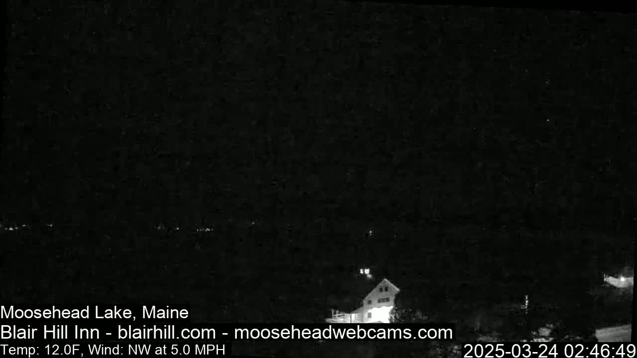 A nighttime, low-light view of a building near a lake with a northwest wind at 5 mph and a temperature of 12°F.