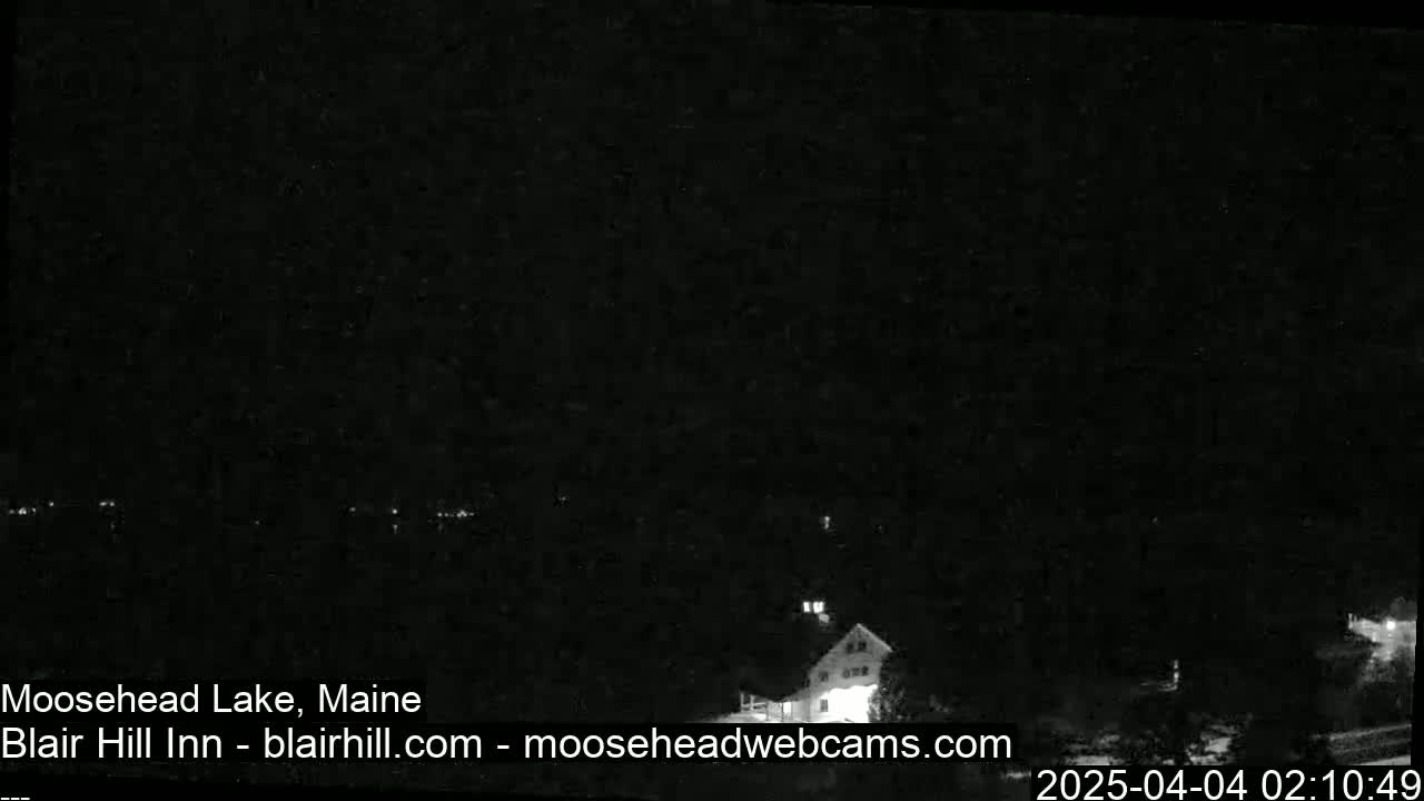 A nighttime, low-light view of a lake and a building, possibly a lodge, under a dark sky.