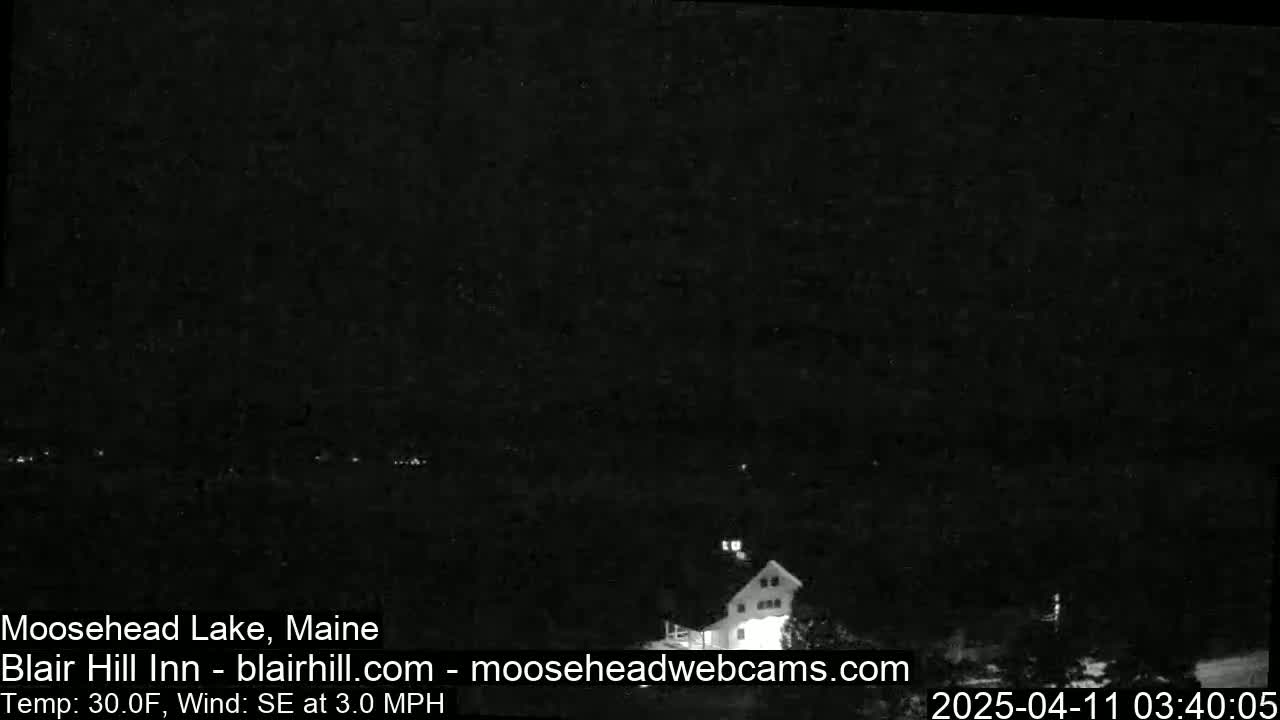 A nighttime, low-light image shows a building near a dark body of water under a clear sky, with a southeast wind at 3 mph and a temperature of 30°F.