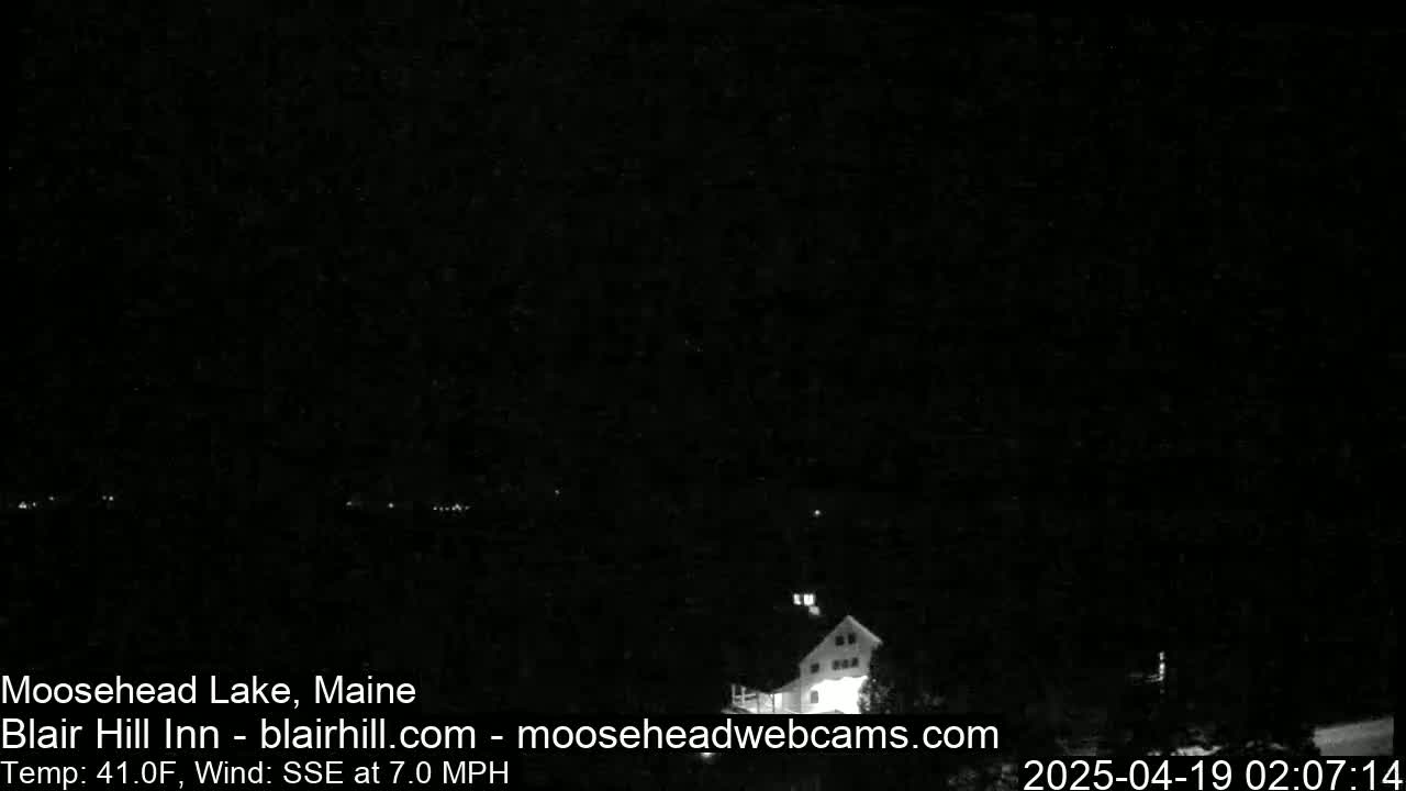 A nighttime, low-light view of a lake and a building under a dark, clear sky with a 7 mph wind from the south-southeast and a temperature of 41°F.