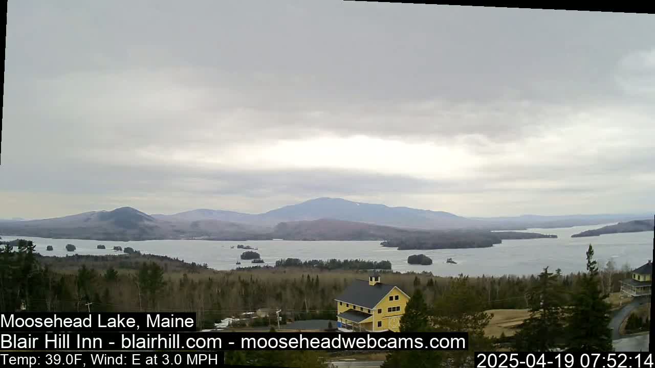 A view of a lake and mountains under an overcast sky, with a yellow building visible in the foreground.