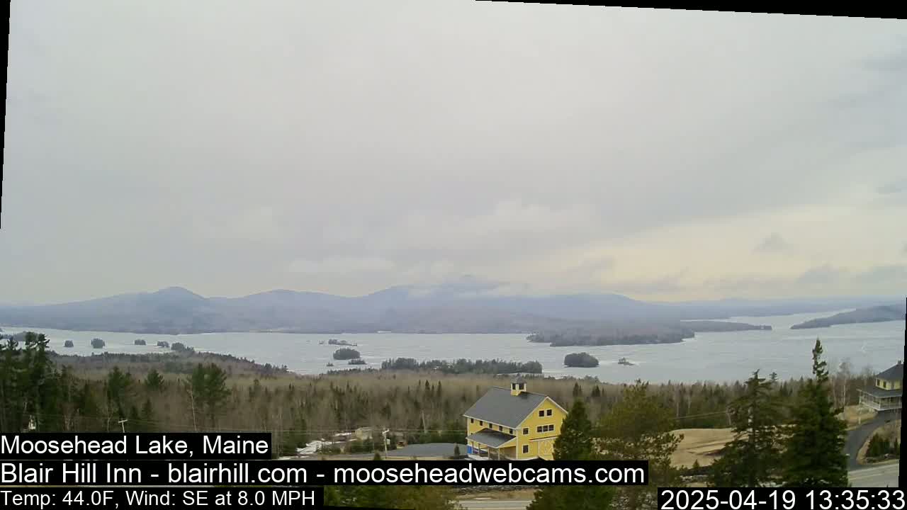 A large lake with numerous islands is visible under an overcast sky, with a yellow building and surrounding trees in the foreground.