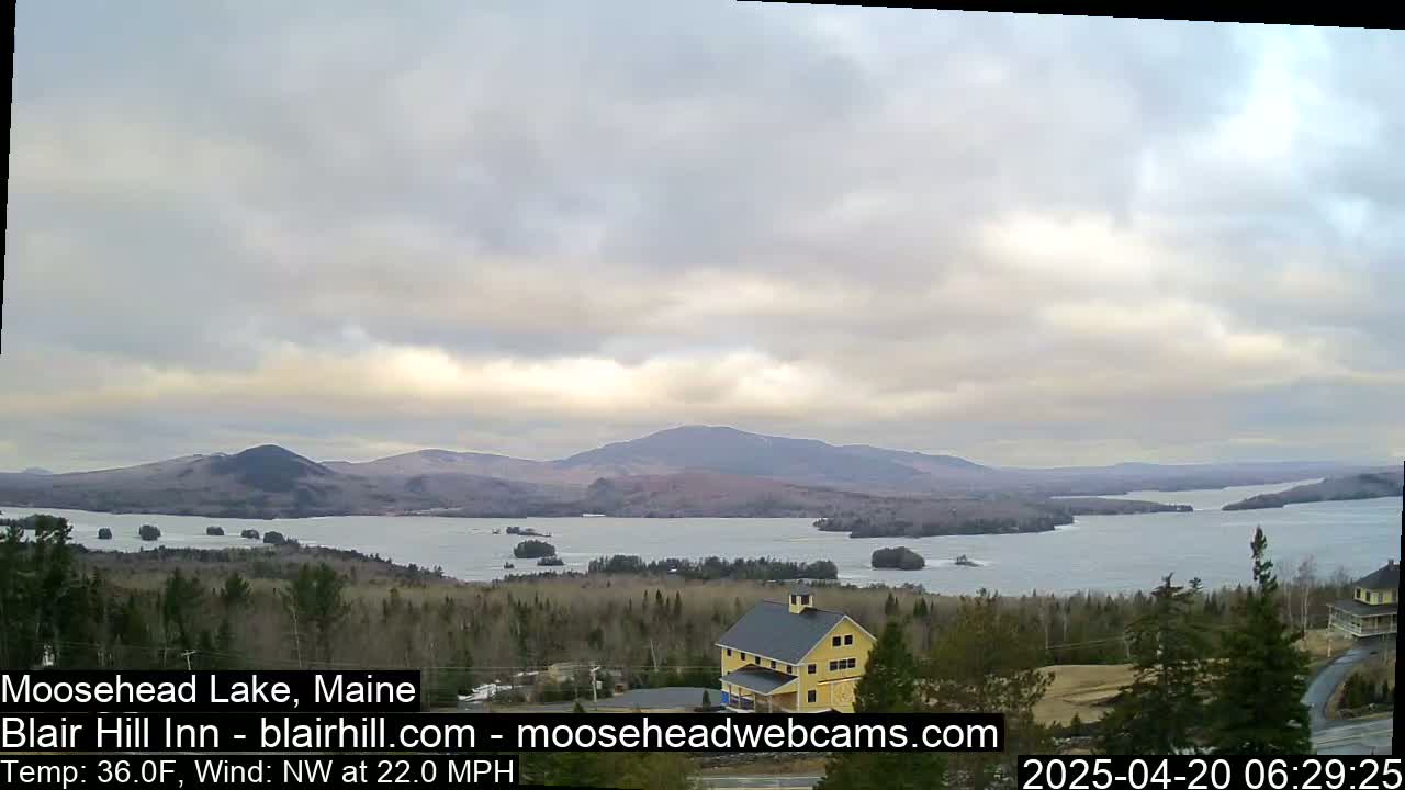 A large lake with islands and distant mountains is visible under an overcast sky, with a building and trees in the foreground.