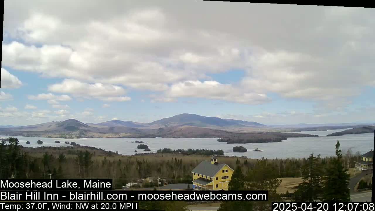 A large lake is nestled between mountains under a partly cloudy sky, with a yellow building visible in the foreground.