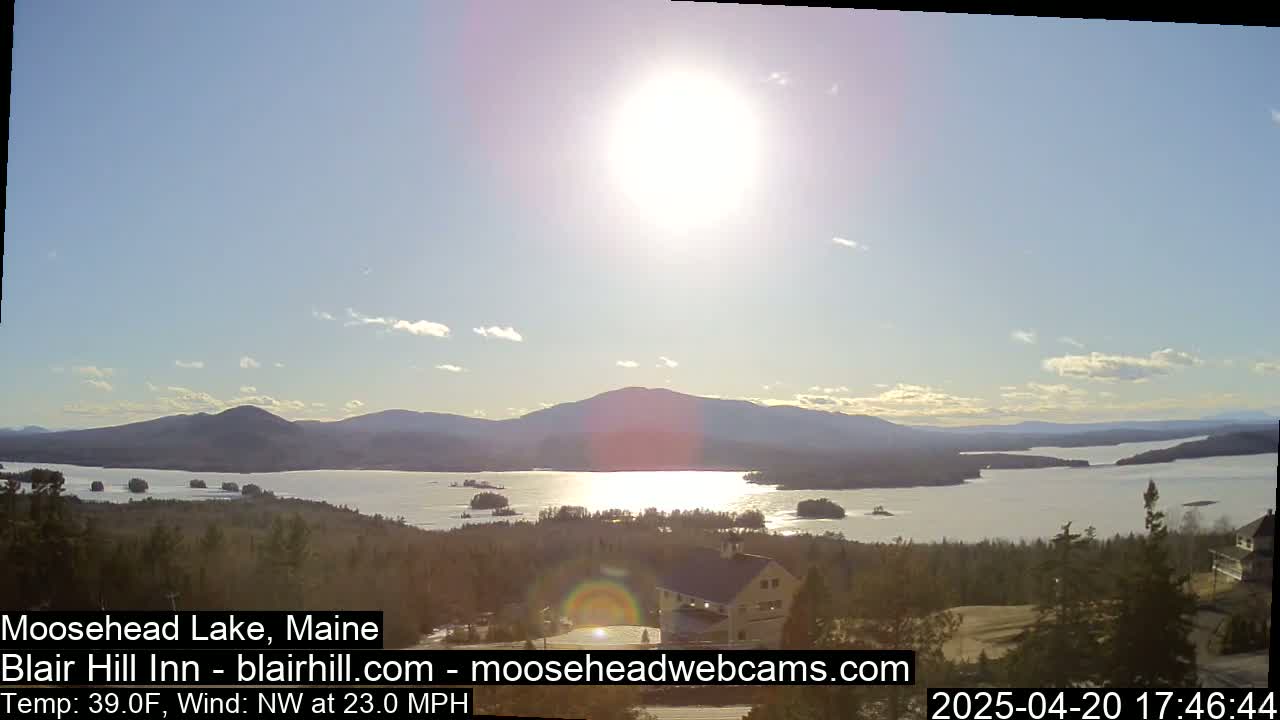 A sunny, windy day overlooks a large lake surrounded by mountains and evergreen trees, with a building visible in the foreground.